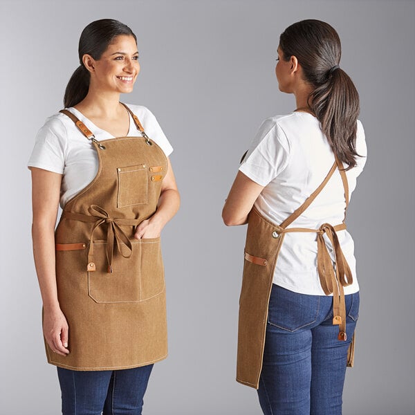 A brown heavy weight canvas cross-back bib apron with three pockets, shown from the front and back on a person.