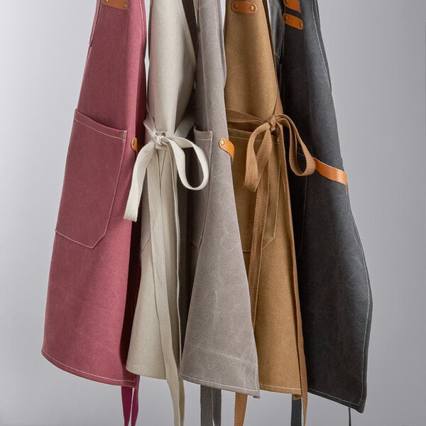 A set of heavy weight canvas cross-back bib aprons in various colors, each with three pockets and adjustable ties.