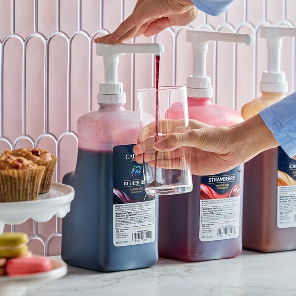 A 64 fl. oz. bottle of Capora Blueberry Flavoring Sauce with a pump dispenser being used to pour sauce into a glass.