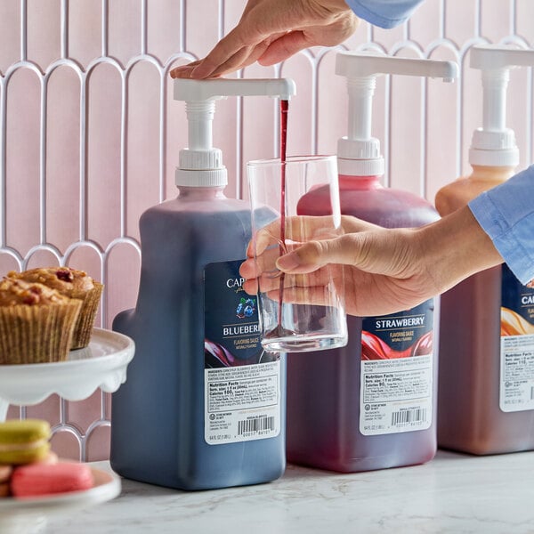 A large pump bottle of Capora Blueberry Flavoring Sauce being dispensed into a glass.