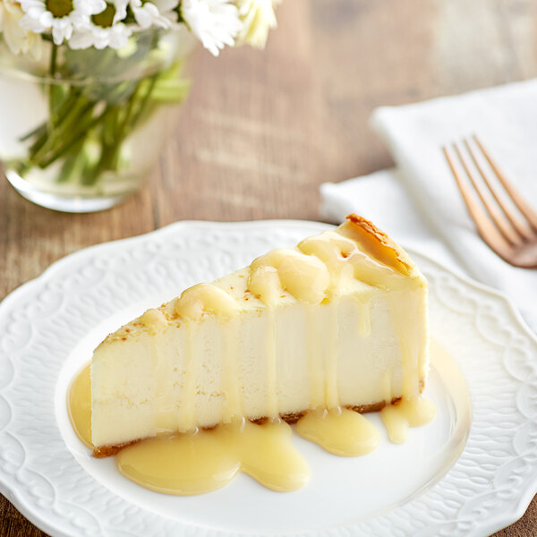 A slice of cheesecake topped with white chocolate sauce on a white plate.
