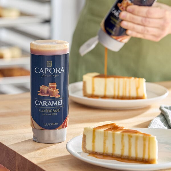 A 12 fl. oz. bottle of Capora Caramel Flavoring Sauce placed on a table next to cheesecake slices being drizzled with caramel sauce.