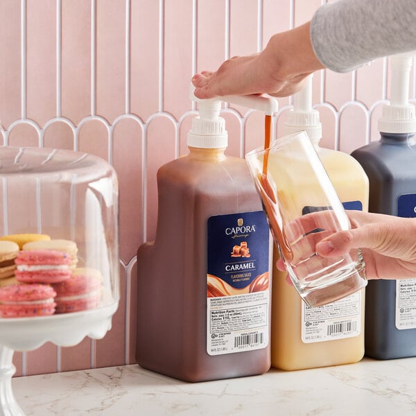 A large pump bottle of Capora Caramel Flavoring Sauce being dispensed into a glass.