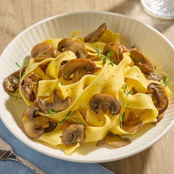 A bowl of wide pasta noodles topped with sliced sautéed mushrooms and garnished with herbs.