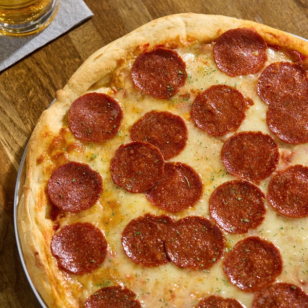 A pizza topped with vegan pepperoni slices and melted cheese on a wooden table.