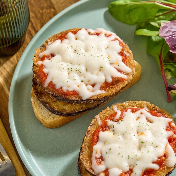 A plate of bread topped with breaded eggplant slices, tomato sauce, and melted dairy-free vegan shredded mozzarella cheese.