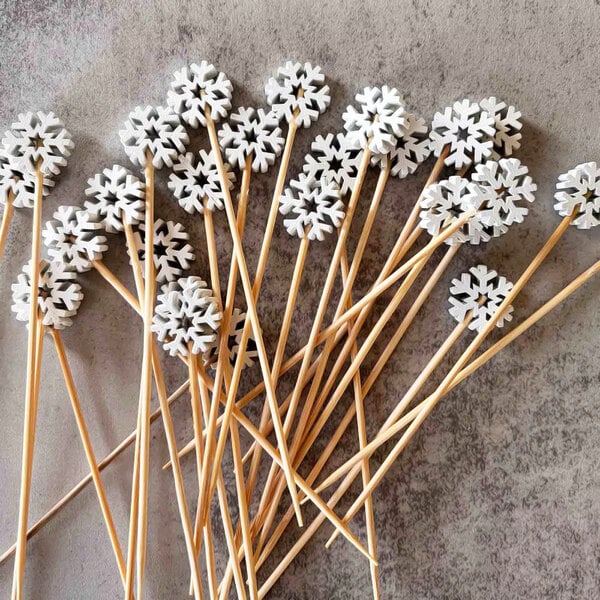 A set of bamboo cocktail picks with white snowflake decorations on top.