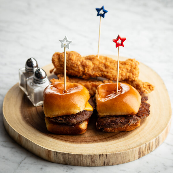 A set of two mini burgers and two fried chicken tenders on a wooden serving board, each burger secured with a red, white, or blue star-topped bamboo pick.