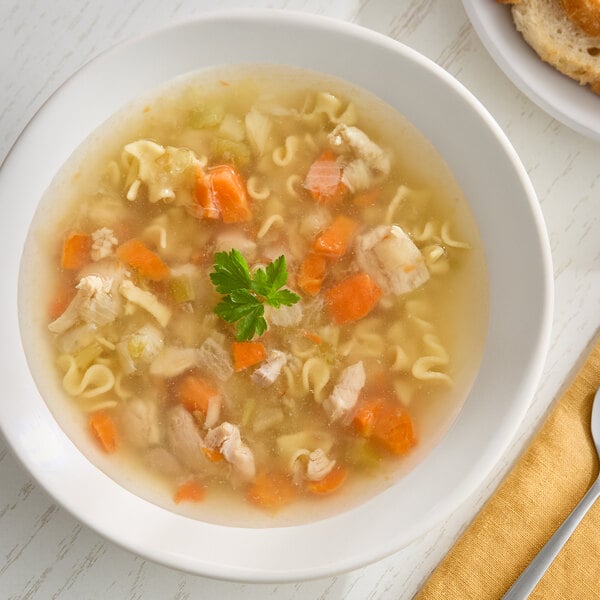 A bowl of chicken noodle soup with pieces of chicken, carrots, celery, and noodles, garnished with parsley.