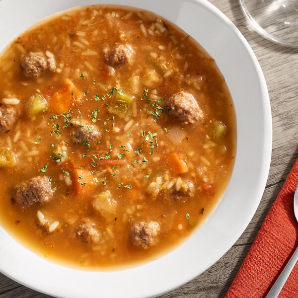 A bowl of albondigas soup with meatballs, rice, and vegetables in a tomato-based broth.