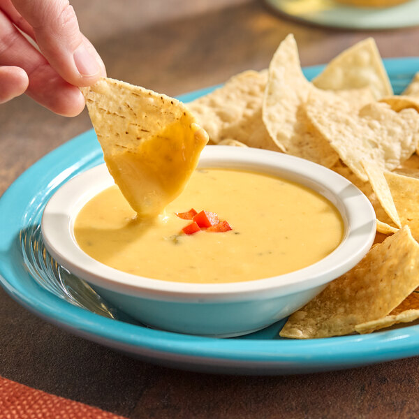 A bowl of creamy queso dip garnished with diced red peppers, served with tortilla chips on a blue plate.