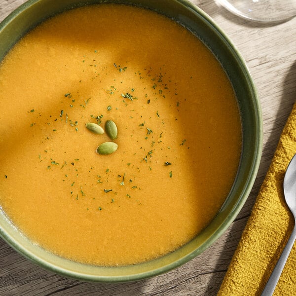 A bowl of butternut squash and apple soup garnished with herbs and pumpkin seeds.