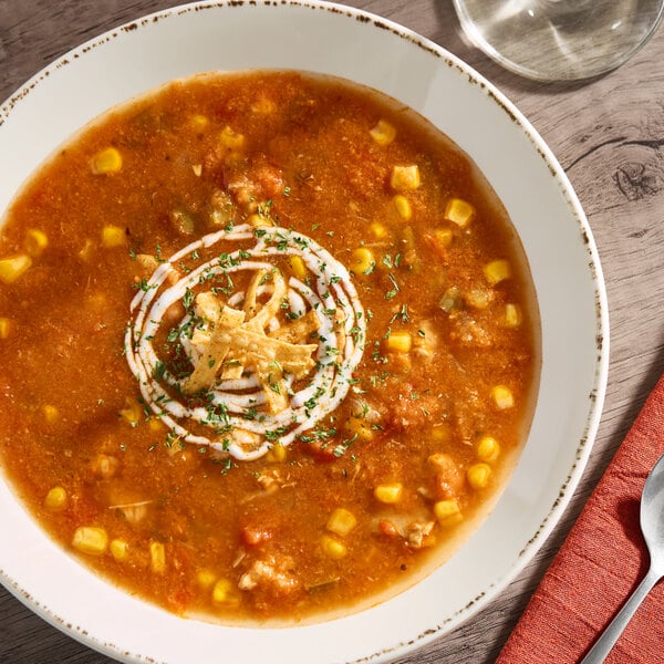 A bowl of chicken tortilla soup garnished with tortilla strips, sour cream, and herbs.