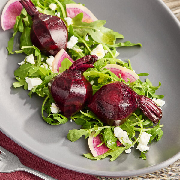 A plate of hand-peeled red baby beets served on a bed of arugula with sliced radishes and crumbled cheese.