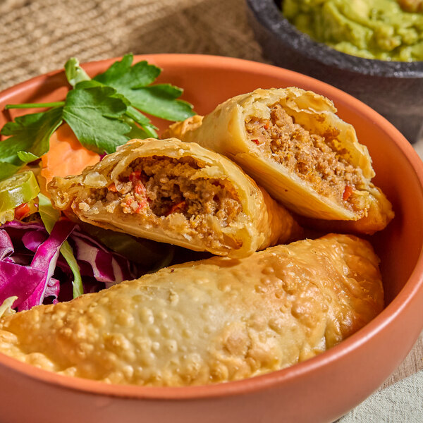 A plate of Brisas beef empanadas with a flour shell, served with a side of fresh vegetables.