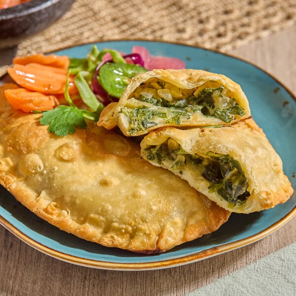 A spinach and cheese empanada with a golden flour shell, served on a plate with pickled vegetables and greens.