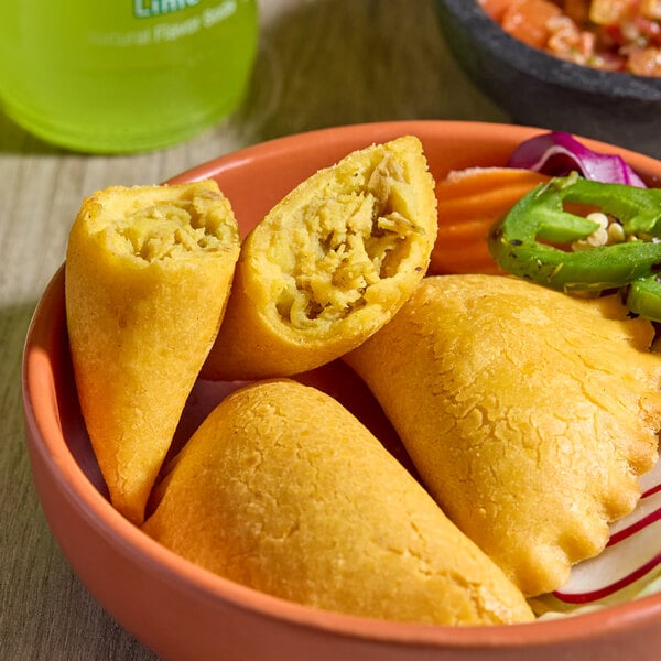 A bowl containing three chicken-filled corn shell empanadas, with one cut open to show the filling.