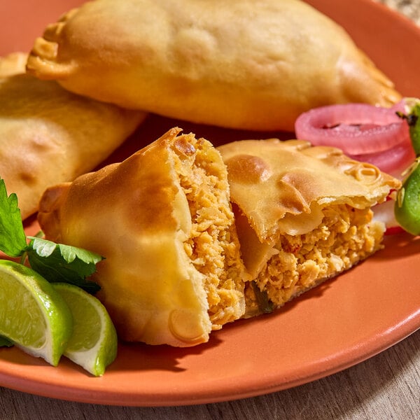 A plate of Brisas chicken flour shell empanadas, with one empanada cut open to show the chicken filling, garnished with lime wedges and herbs.