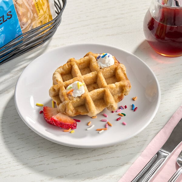 A single vegan birthday cake protein Liege waffle topped with whipped cream, colorful sprinkles, and a strawberry slice on a white plate.