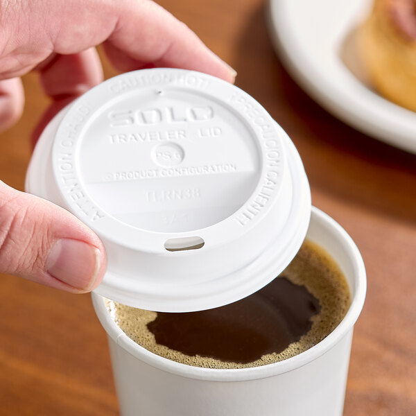 A white plastic Solo Traveler lid being placed on a disposable coffee cup.