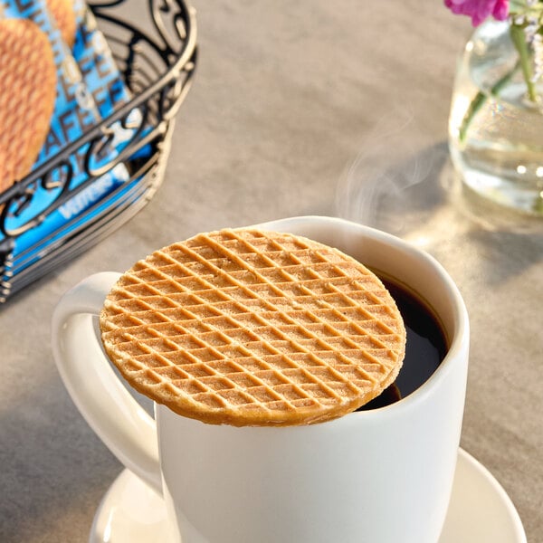 A round vegan gluten-free caramel stroopwafel resting on top of a white mug filled with hot coffee.