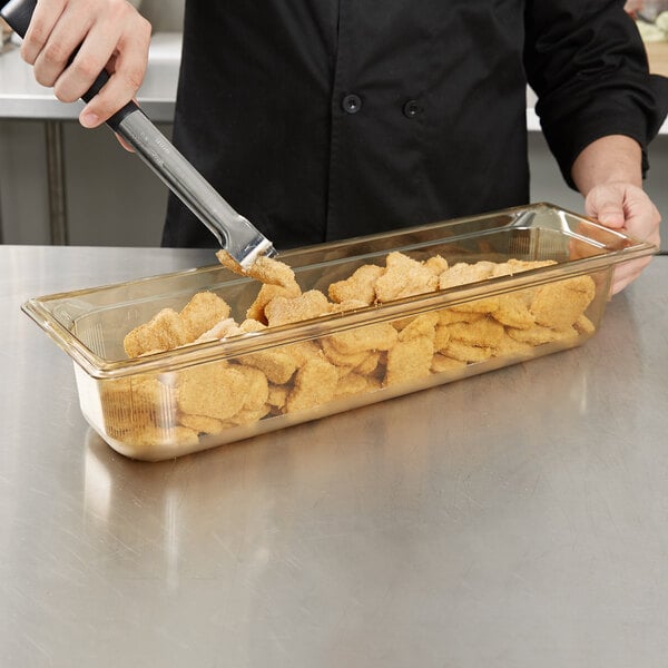 A person using a Vollrath amber plastic food pan to hold chicken nuggets.