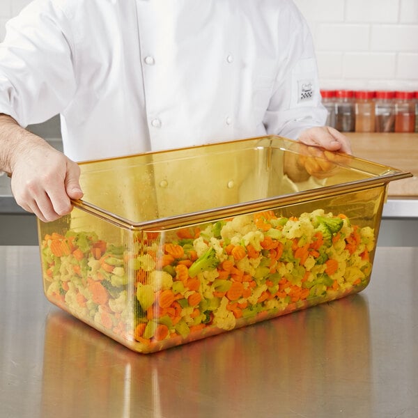 A chef holding a Vollrath amber plastic food pan filled with vegetables.