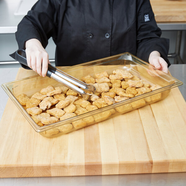 A person using a knife to cut chicken nuggets on a Vollrath amber plastic food pan.