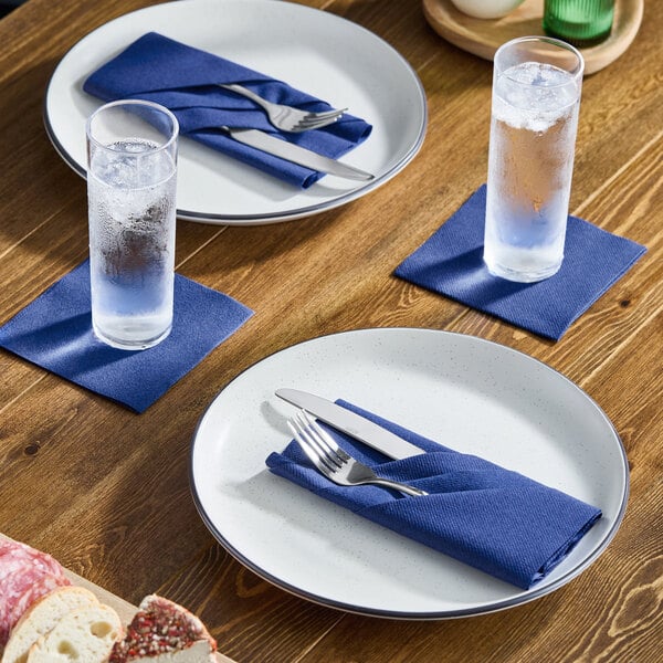 A navy blue airlaid linen-feel paper napkin placed on a dining table setting with plates, cutlery, and glasses.