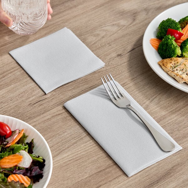 A gray airlaid linen-feel dinner napkin folded on a table with a fork placed on top.