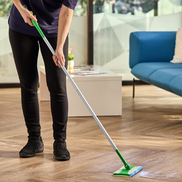 A Swiffer Sweep and Mop floor mopping and sweeping kit with a green and white handle being used to clean a wooden floor.
