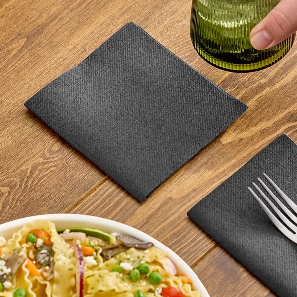 A black linen-feel beverage napkin folded into a square, placed on a wooden table.