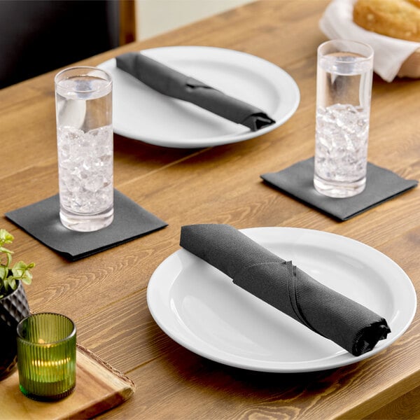 A set of black linen-feel 1/4 fold beverage napkins placed under glasses and on plates on a wooden dining table.
