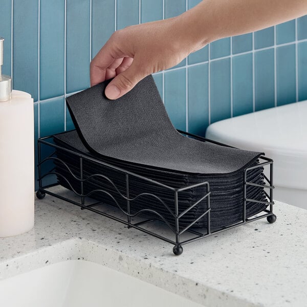 A stack of black linen-feel guest towels in a metal holder on a bathroom counter.
