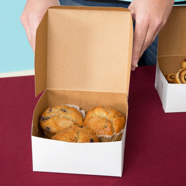 A white bakery box containing three muffins with the lid open.