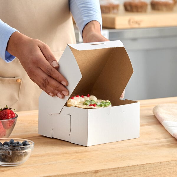 A white, customizable bakery box being closed around a decorated pie or pastry.