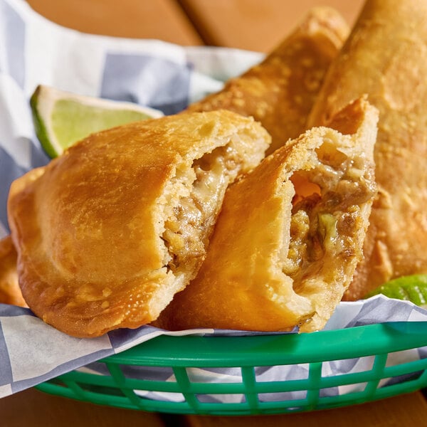 A golden-brown flour shell empanada filled with short rib, shown in a basket with a lime wedge.
