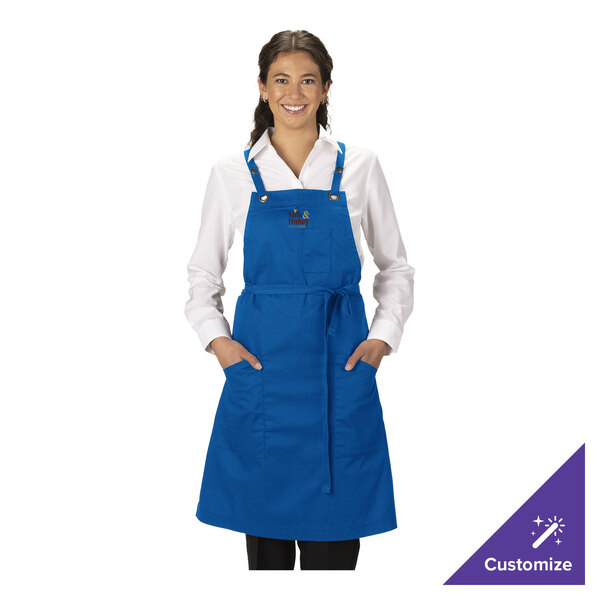 A royal blue customizable poly/cotton cross-back bib apron with three pockets, measuring 34 by 28 inches.