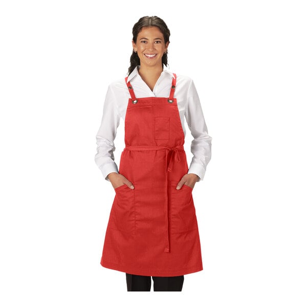 A red poly/cotton cross-back bib apron with three pockets, shown on a person wearing a white shirt.
