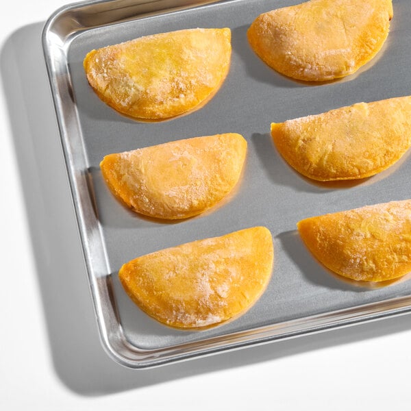 A tray of frozen beef and potato corn shell empanadas arranged in rows.