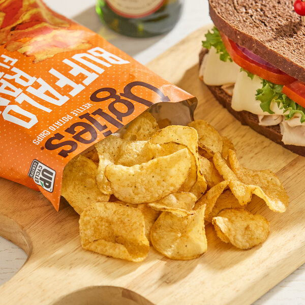A bag of Uglies Buffalo Ranch Kettle Potato Chips with chips spilled onto a wooden board next to a sandwich.
