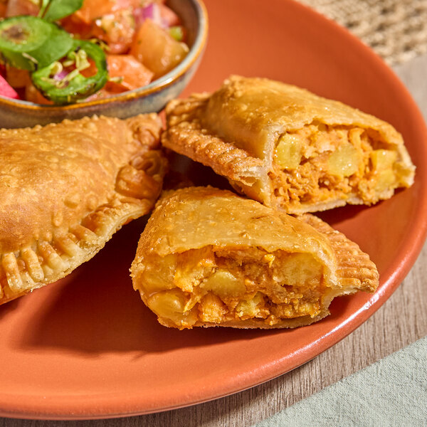 A plate of chicken sofrito empanadas with a flour shell, served with a side of salsa.