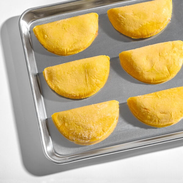 A baking tray with six frozen mozzarella cheese corn shell empanadas.