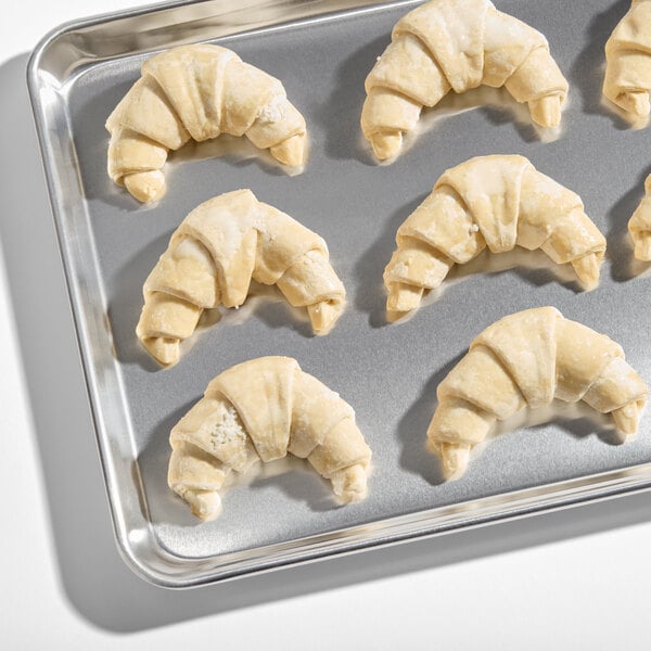 A baking tray with several unbaked, curved croissants arranged on it.