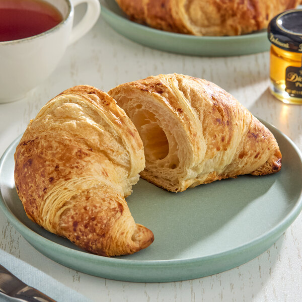 A golden, flaky croissant cut in half and served on a light blue plate.