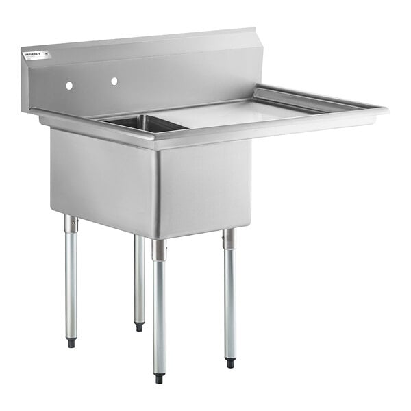 A stainless steel commercial sink with four metal legs, a single deep basin, a right-side drainboard, and a backsplash with faucet holes.