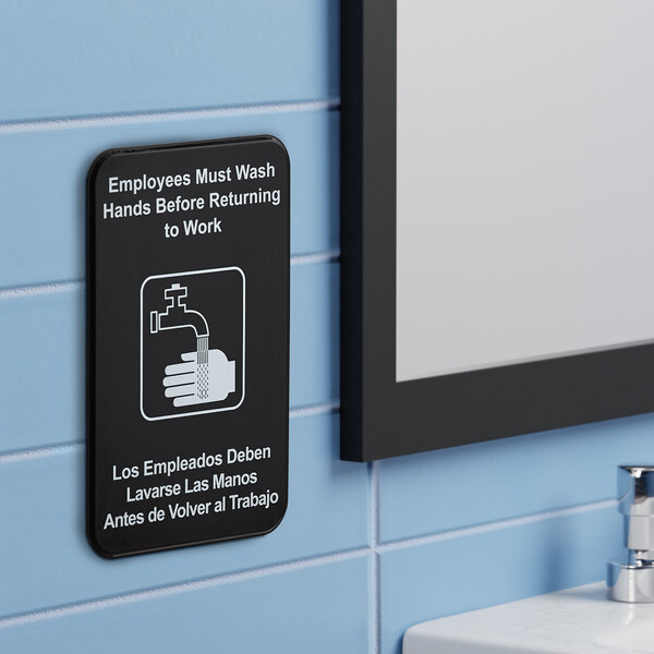 A black and white bilingual sign that instructs employees to wash their hands before returning to work.