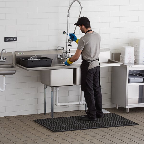 A stainless steel two-compartment commercial sink with two drainboards and galvanized steel legs, shown in use in a kitchen setting.