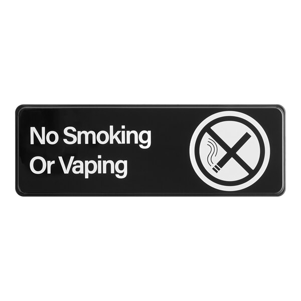 A rectangular black and white sign that reads 'No Smoking Or Vaping' with a crossed-out cigarette symbol.