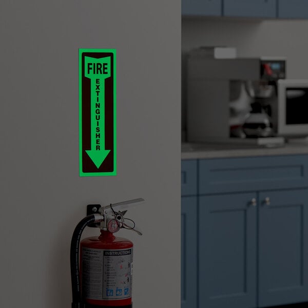 A glow-in-the-dark adhesive vinyl safety label with a down arrow indicating the location of a fire extinguisher.
